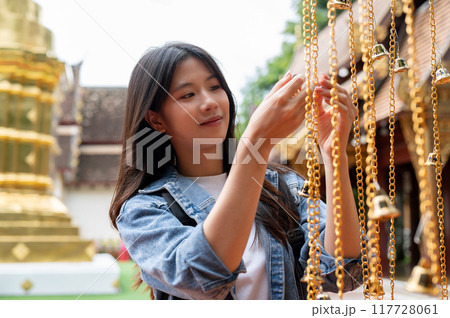 A positive Asian female tourist is hanging a bell for luck in a temple during her visit to Thailand. A positive Asian female tourist is hanging a bell for luck in a temple during her visit to Thailand. 117728061