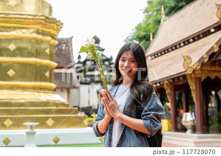 A charming Asian female tourist is making a wish while visiting a temple in Thailand. 117728070