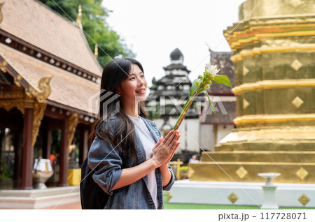 A charming Asian female tourist is making a wish while visiting a temple in Thailand. 117728071