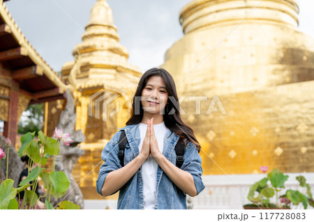 An attractive Asian female tourist is putting her hands together in a prayer position in a temple. An attractive Asian female tourist is putting her hands together in a prayer position in a temple. 117728083
