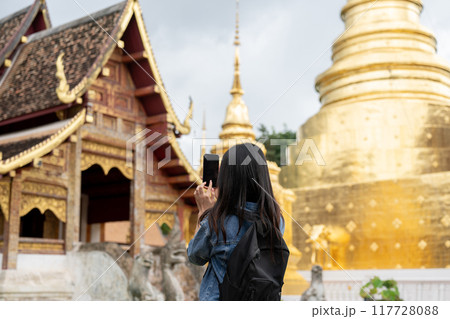 A back view of an Asian female tourist taking a picture of a stunning temple with her smartphone. A back view of an Asian female tourist taking a picture of a stunning temple with her smartphone. 117728088