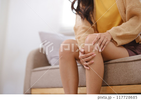 A woman sits on a couch with her knee propped up 117728685