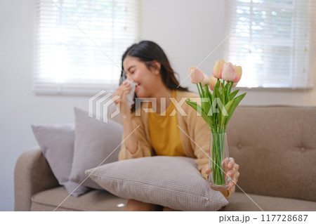 A woman is sitting on a couch with a vase of flowers in her hand A woman is sitting on a couch with a vase of flowers in her hand 117728687