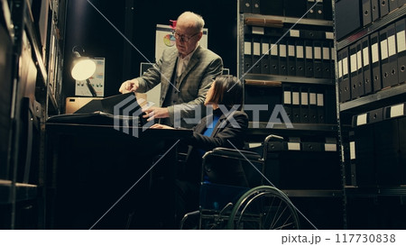 Forensic team identifying patterns in criminal behavior by analyzing archived records and witness statements, disability friendly incident room. Detectives confirm or cross check data. Camera B. 117730838