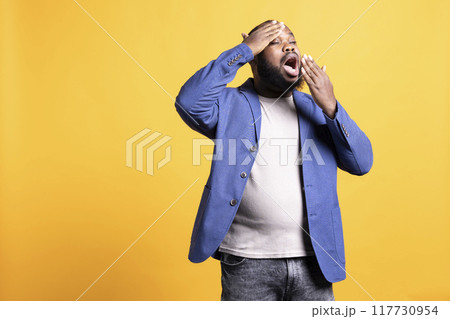 African american man feeling exhausted from overworking, suffering from headache and yawning, isolated over studio background. Tired BIPOC person feeling pain from fatigue African american man feeling exhausted from overworking, suffering from headache and yawning, isolated over studio background. Tired BIPOC person feeling pain from fatigue 117730954