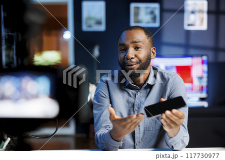 African american internet star being sponsored by partnering brand to do smartphone unboxing content. Tech expert does influencer marketing, doing product placement of mobile phone 117730977