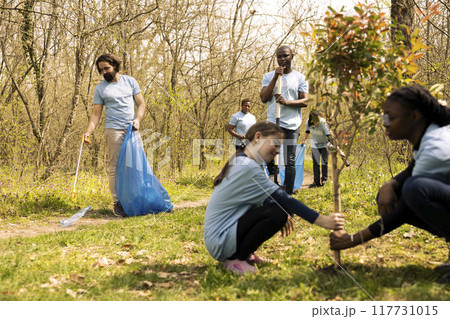 Diverse team of climate activists picking up garbage from the ground, collecting rubbish and recycling plastic in bags. People tidying the forest environment from trash, illegal dumping. Diverse team of climate activists picking up garbage from the ground, collecting rubbish and recycling plastic in bags. People tidying the forest environment from trash, illegal dumping. 117731015