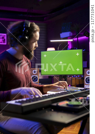 Musician learning to play electronic keyboard synthesizer in home studio, watching tutorial online via greenscreen on computer. Music composer playing midi controller notes, rehearsal practice. Musician learning to play electronic keyboard synthesizer in home studio, watching tutorial online via greenscreen on computer. Music composer playing midi controller notes, rehearsal practice. 117731041
