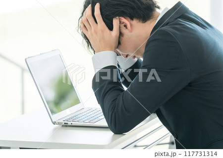 デスクで頭を抱えながら悩む若い男性ビジネスマン 117731314