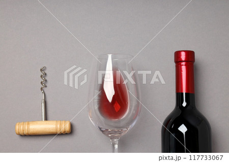 A bottle of wine, a glass and a corkscrew, on a gray background. 117733067