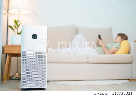 Air Purifier with woman relax and use smartphone on sofa. Purification system for filter and cleaning dust PM2.5 HEPA and virus in home. Allergy, Pure air, health, Wellness lifestyle and Air Pollution 117733321