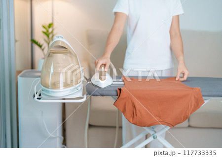 Woman hold Electric hot iron press T shirt clothes on ironing board, Intelligent automatic steam iron. Laundry, Housework, Housekeeping, Domestic hygiene, household of chores and daily routine concept Woman hold Electric hot iron press T shirt clothes on ironing board, Intelligent automatic steam iron. Laundry, Housework, Housekeeping, Domestic hygiene, household of chores and daily routine concept 117733335