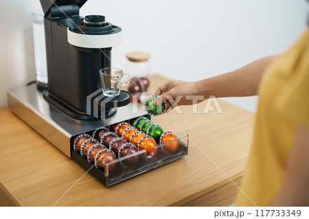 hand making Espresso Coffee by Coffee Maker Machine with Capsule of roasted coffee bean on wood table bar. Daily beverage drink at Home, Apartment and Office concept 117733349