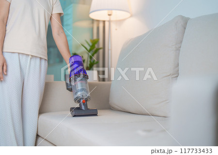Woman cleaning Sofa with cordless Vacuum cleaner. Housewife using wireless Vacuum for big cleaning home. Housework, Housecleaning, Housekeeping, Removes dust, Domestic hygiene and daily routine 117733433