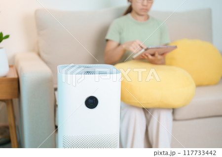 Air Purifier with woman relax and use tablet on sofa. Purification system for filter and cleaning dust PM2.5 HEPA and virus in home. Allergy, Pure air, health, Wellness lifestyle and Air Pollution 117733442