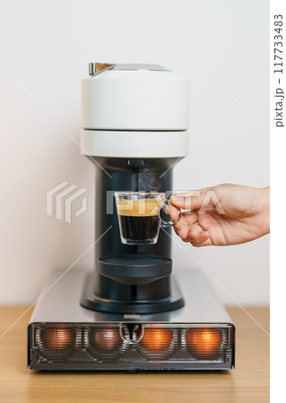 hand making Espresso Coffee by Coffee Maker Machine with Capsule of roasted coffee bean on wood table bar. Daily beverage drink at Home, Apartment and Office concept hand making Espresso Coffee by Coffee Maker Machine with Capsule of roasted coffee bean on wood table bar. Daily beverage drink at Home, Apartment and Office concept 117733483