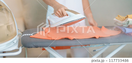 Woman hold Electric hot iron press T shirt clothes on ironing board, Intelligent automatic steam iron. Laundry, Housework, Housekeeping, Domestic hygiene, household of chores and daily routine concept Woman hold Electric hot iron press T shirt clothes on ironing board, Intelligent automatic steam iron. Laundry, Housework, Housekeeping, Domestic hygiene, household of chores and daily routine concept 117733486