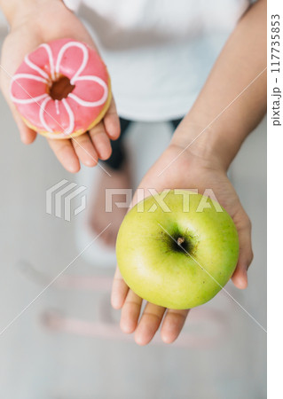 woman on weight scale and hand hold green Apple and donut, choose between fruit is Healthy and sweet is Unhealthy junk food. Dieting control, Weight loss, Obesity, eating lifestyle and nutrition 117735853