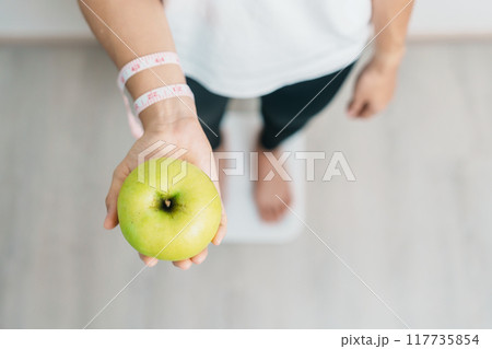 woman on weight scale and hand hold green Apple, choose fruit is Healthy food. Dieting control, Weight loss, Obesity, eating lifestyle and nutrition concepts woman on weight scale and hand hold green Apple, choose fruit is Healthy food. Dieting control, Weight loss, Obesity, eating lifestyle and nutrition concepts 117735854