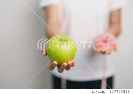 woman hand hold green Apple and donut, female fitness choose between fruit is Healthy and sweet is Unhealthy junk food. Dieting control, Weight loss, Obesity, eating lifestyle and nutrition concept woman hand hold green Apple and donut, female fitness choose between fruit is Healthy and sweet is Unhealthy junk food. Dieting control, Weight loss, Obesity, eating lifestyle and nutrition concept 117735858
