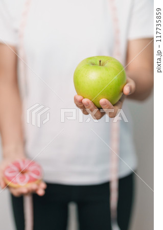 woman hand hold green Apple and donut, female fitness choose between fruit is Healthy and sweet is Unhealthy junk food. Dieting control, Weight loss, Obesity, eating lifestyle and nutrition concept woman hand hold green Apple and donut, female fitness choose between fruit is Healthy and sweet is Unhealthy junk food. Dieting control, Weight loss, Obesity, eating lifestyle and nutrition concept 117735859