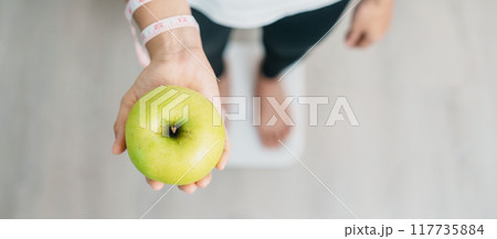 woman on weight scale and hand hold green Apple, choose fruit is Healthy food. Dieting control, Weight loss, Obesity, eating lifestyle and nutrition concepts woman on weight scale and hand hold green Apple, choose fruit is Healthy food. Dieting control, Weight loss, Obesity, eating lifestyle and nutrition concepts 117735884