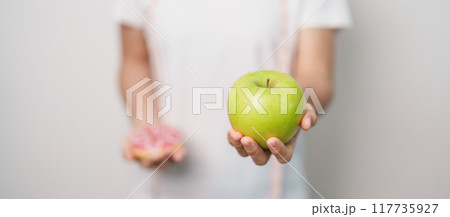 woman hand hold green Apple and donut, female fitness choose between fruit is Healthy and sweet is Unhealthy junk food. Dieting control, Weight loss, Obesity, eating lifestyle and nutrition concept woman hand hold green Apple and donut, female fitness choose between fruit is Healthy and sweet is Unhealthy junk food. Dieting control, Weight loss, Obesity, eating lifestyle and nutrition concept 117735927