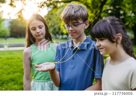 Children in outdoor sustainable educational class using compass learning orienteering in public park. 117736008