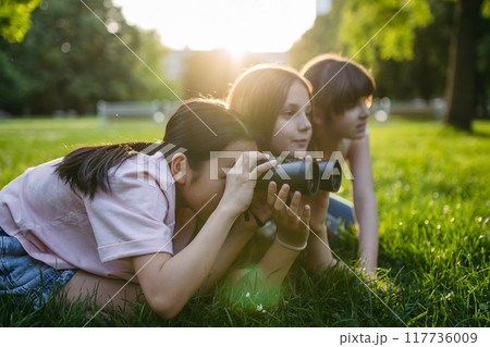 Young girl students learning about nature and wildlife in urban environment, using binoculars and observing animals in public park. 117736009