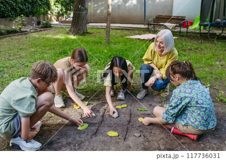 Students playing tic-tac-toe with stones and leaves, grid in soil. Outdoor sustainable education class. Students playing tic-tac-toe with stones and leaves, grid in soil. Outdoor sustainable education class. 117736031