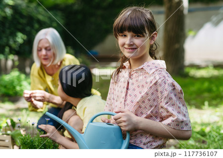 Portrait of cute schoolgirl taking care of plants in school garden during at outdoor sustainable education class. Concept of experiential learning and ecoliteracy. 117736107