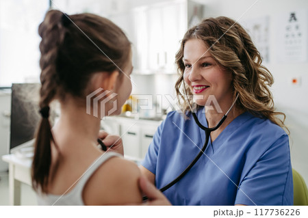 Doctor examining young girl, listening to heartbeat, breathing, using stethoscope. School entry medical exam. Doctor examining young girl, listening to heartbeat, breathing, using stethoscope. School entry medical exam. 117736226