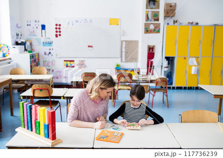 Teacher using geoboard in class, teaching students, explaining geometry, shapes, fractions or patterns. Using education tools in elementary school. 117736239