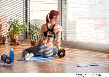 Beautiful redhead woman's home workout routine with dumbbell. Home fitness workout in living room, sporty woman wearing sportswear. Beautiful redhead woman's home workout routine with dumbbell. Home fitness workout in living room, sporty woman wearing sportswear. 117736266