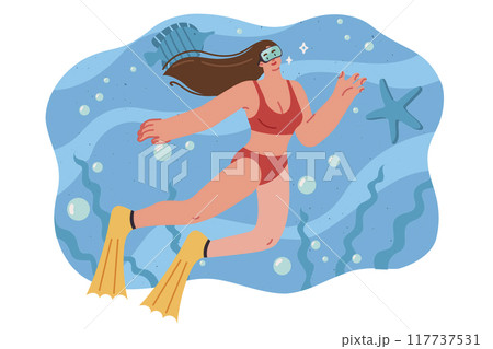 Woman is engaged in diving, swimming underwater among fish and sea plants, dressed in swimsuit 117737531