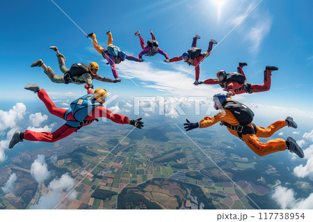 Group of skydivers in mid-air, creating circular formation while descending over picturesque landscape on sunny day with clear blue sky and scattered clouds 117738954
