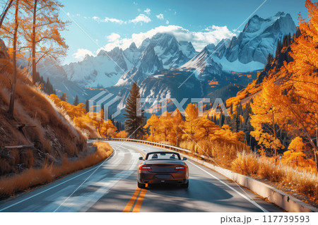 Convertible car driving along winding mountain road surrounded by vibrant autumn foliage and snowy peaks in distance, capturing essence of seasonal beauty and adventure 117739593