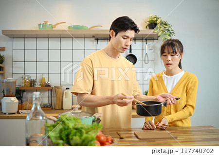 Happy young couple preparing meal together with fresh ingredients in minimalist kitchen 117740702