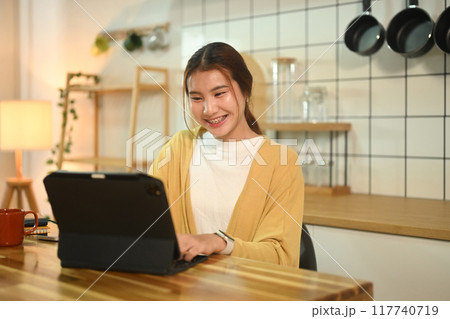 Happy young asian woman working on digital tablet at a kitchen counter 117740719