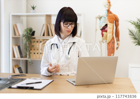 Female doctor examining medication bottle in modern office Female doctor examining medication bottle in modern office 117743836