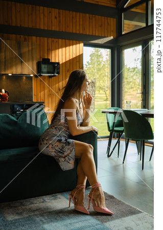 Elegant pensive woman sitting on green sofa in log cabin and looking to the window Elegant pensive woman sitting on green sofa in log cabin and looking to the window 117744753