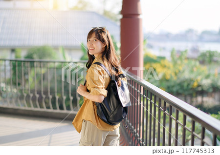 Unveiling the beauty of Bangkok, a smiling Asian woman in her 30s embarks on a solo journey of exploration. Backpack on, camera ready, she captures the essence of urban adventure. 117745313