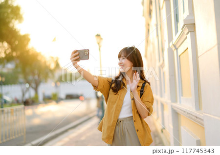 Traveler asian woman in her 30s making a livestream and sefie with a smartphone enjoying travel in Bangkok, Thailand. Journey trip lifestyle, world travel explorer or Asia summer tourism concept. Traveler asian woman in her 30s making a livestream and sefie with a smartphone enjoying travel in Bangkok, Thailand. Journey trip lifestyle, world travel explorer or Asia summer tourism concept. 117745343