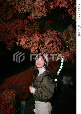 Asian woman in a chic jacket, experiencing the magic of Christmas in Japan's urban night. A festive portrait amidst snow and nature's vibrant beauty. 117745385