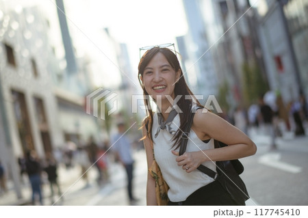 Japanese urban lifestyle, a young Asian woman stands at a road corner, a stylish tote bag enhancing her casual and trendy look. Copy space included. Japanese urban lifestyle, a young Asian woman stands at a road corner, a stylish tote bag enhancing her casual and trendy look. Copy space included. 117745410