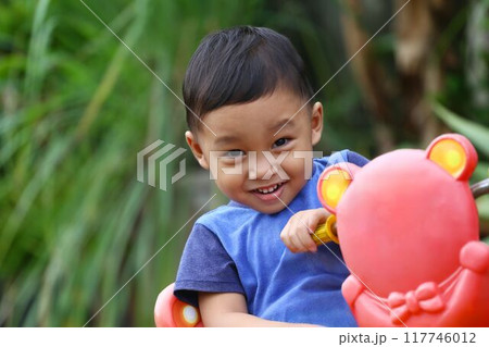 Asian boy about two years old wear a blue shirt was sitting on his toy car. 117746012