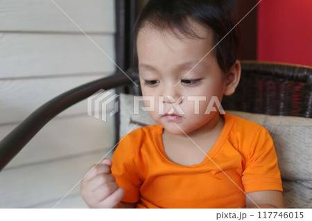 Asian boy about two years old in an orange shirt was sitting on chair. 117746015