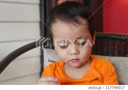 Asian boy about two years old in an orange shirt was sitting on chair. 117746017