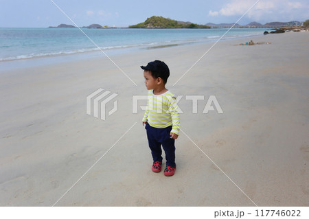 A boy about two years old was wearing a long-sleeved shirt standing on the beach. 117746022