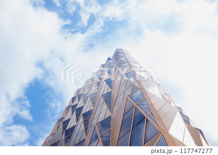 glass golden copper blue futuristic modern skyscraper building facade, wall on cloudy sky. view from below 117747277